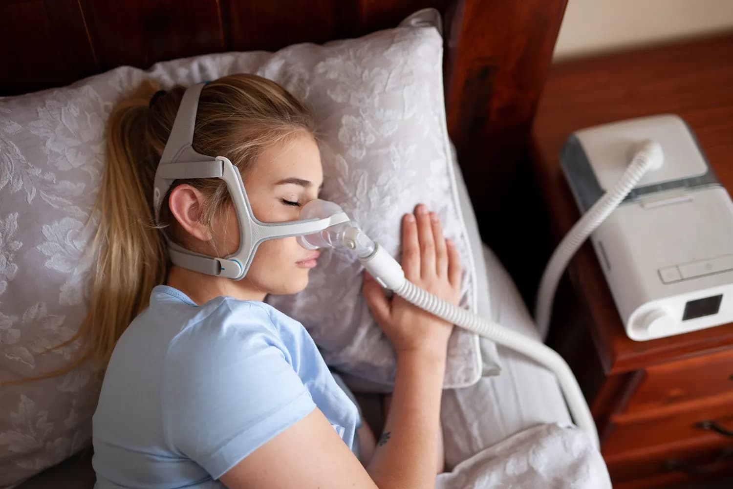 Woman smiling while using a phone and pillow, representing a simpler sleep care experience.